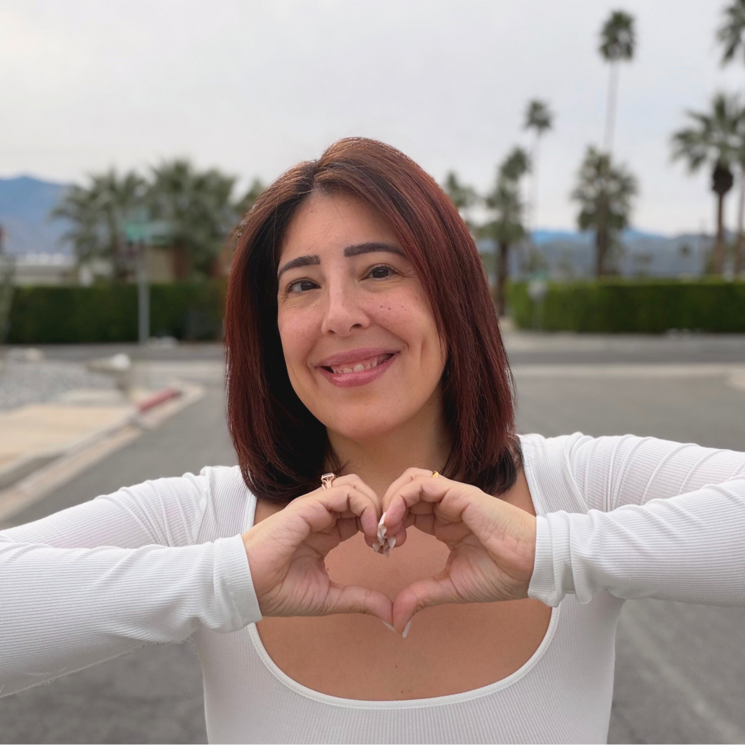 Woman making a heart shape with her hands outdoors with palm trees in the background